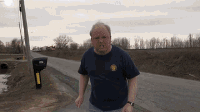 a man in a blue shirt stands on the side of the road