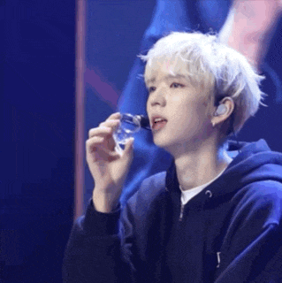 a young man in a black hoodie is holding a glass of water in his hand .