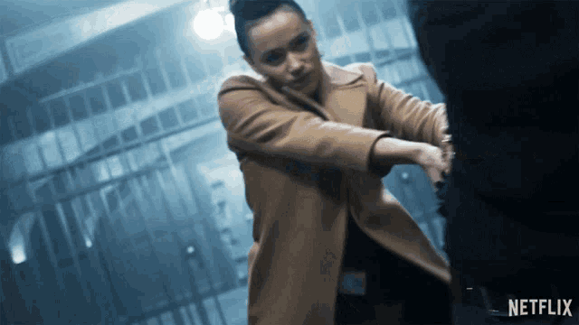 a woman in a tan coat is holding a man 's hand with a netflix logo in the corner