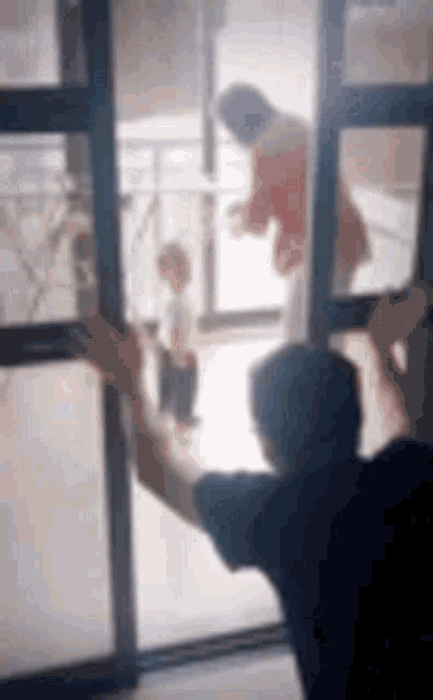 a man is standing in front of a sliding glass door looking out at a child .