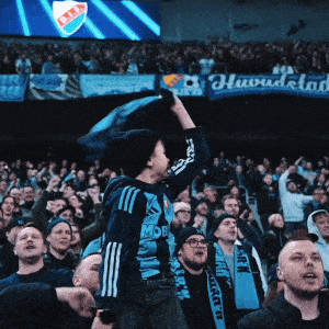 a man in a blue adidas shirt holds up a blue scarf in front of a crowd of people