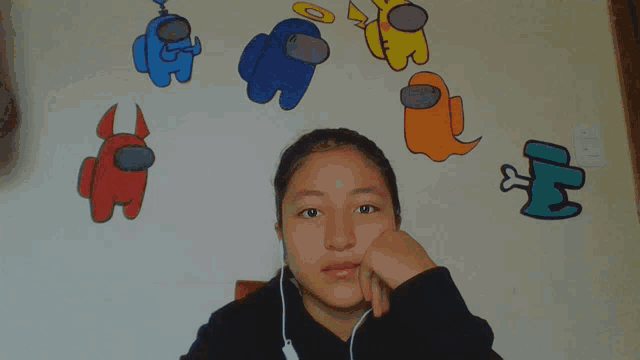 a girl wearing headphones stands in front of among us characters painted on the wall