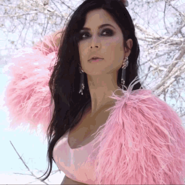 a woman wearing a pink fur coat and earrings looks at the camera
