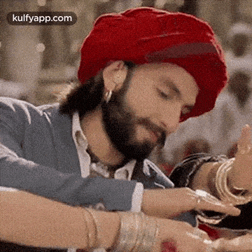 a man with a beard wearing a red turban and bracelets is dancing .