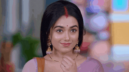 a close up of a woman wearing a purple saree and earrings smiling .