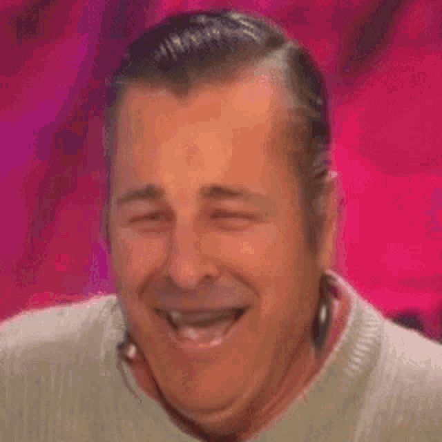 a man in a sweater is laughing with his eyes closed and his mouth open .
