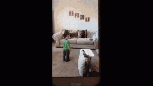 a boy in a green shirt is standing next to a couch in a living room