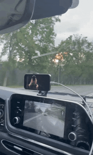 a phone mounted on the dashboard of a car shows a woman walking down the street