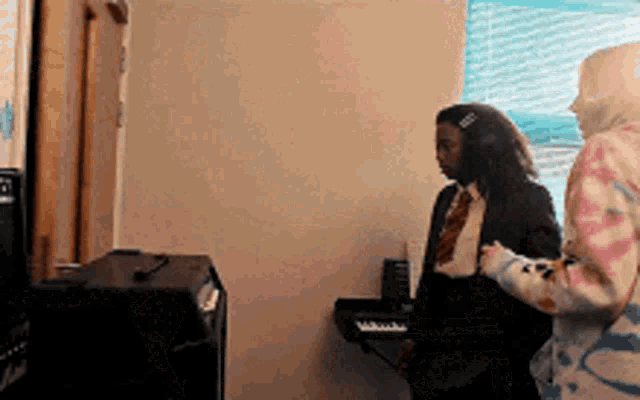 two women are standing next to each other in a room in front of a piano .