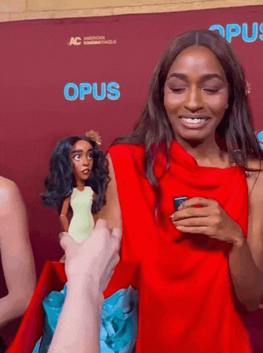 a woman in a red dress is holding a doll in front of a wall that says opus