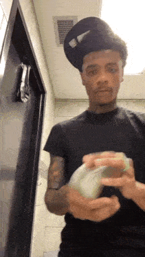 a man in a black shirt and hat is holding a bunch of money in his hands .