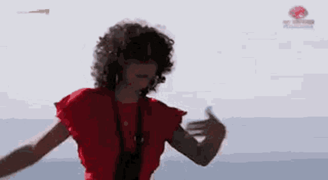 a woman in a red top is dancing in front of the ocean .