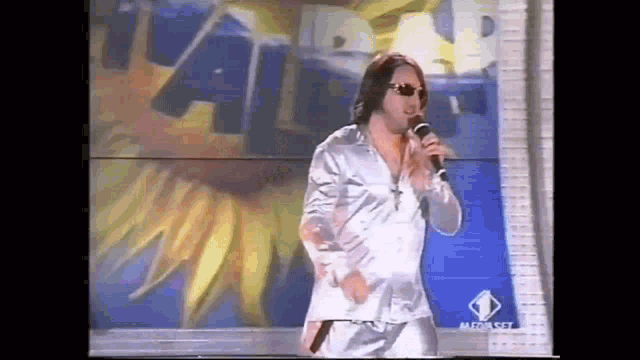 a man is singing into a microphone in front of a sign that says " a "