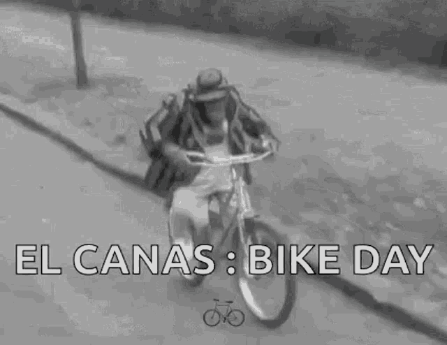 a man is riding a bike down a street with the words `` el canas bike day '' above him .