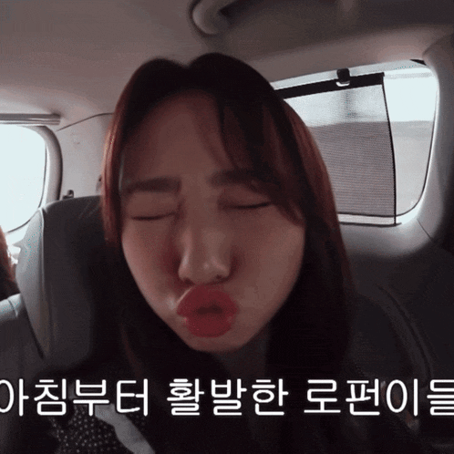 a woman making a face with her eyes closed in a car with korean writing on the bottom