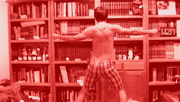 a man without a shirt is dancing in front of a bookshelf with a sign that says k2m