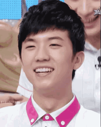 a close up of a young man wearing a white shirt with a pink collar smiling .