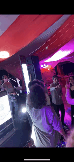 a group of people are dancing in a room with purple lights on the ceiling