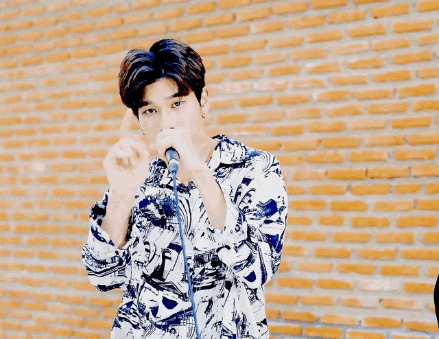 a young man is singing into a microphone with a brick wall in the background
