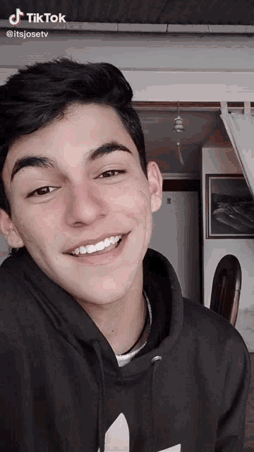 a young man wearing a black hoodie is smiling for the camera