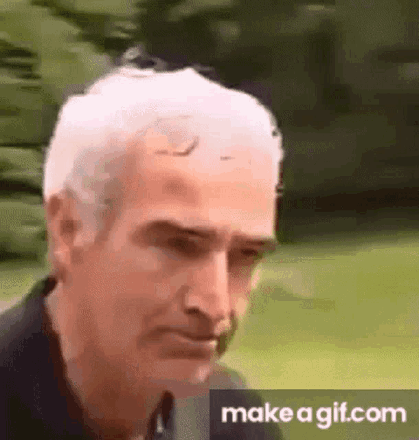 a man with gray hair is making a funny face while standing in the grass .