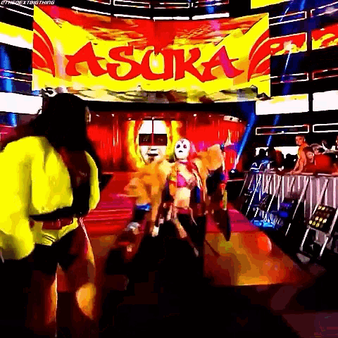 a couple of women are standing in front of a sign that says asuka on it .