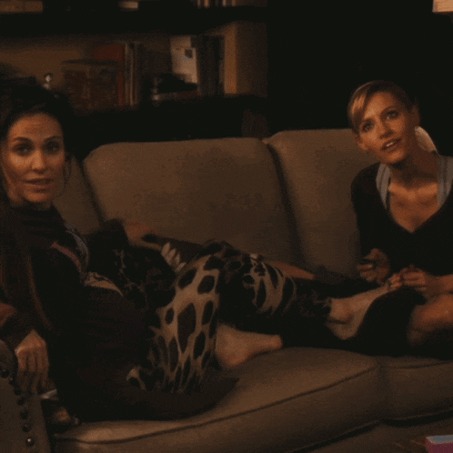two women are sitting on a couch with their feet on the couch