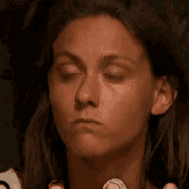 a close up of a woman 's face with her eyes closed and her hands on her neck .