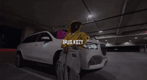 a man in a yellow hoodie is standing next to a white car in a parking lot