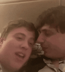 two young men are sitting next to each other on a bed and talking to each other .