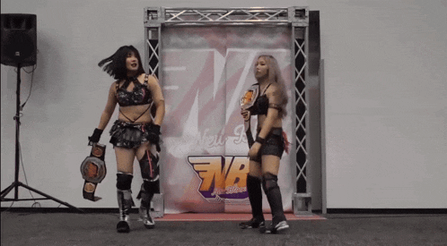 two female wrestlers standing in front of a sign that says nb