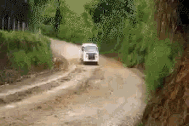 a white van is driving down a dirt road in the woods .