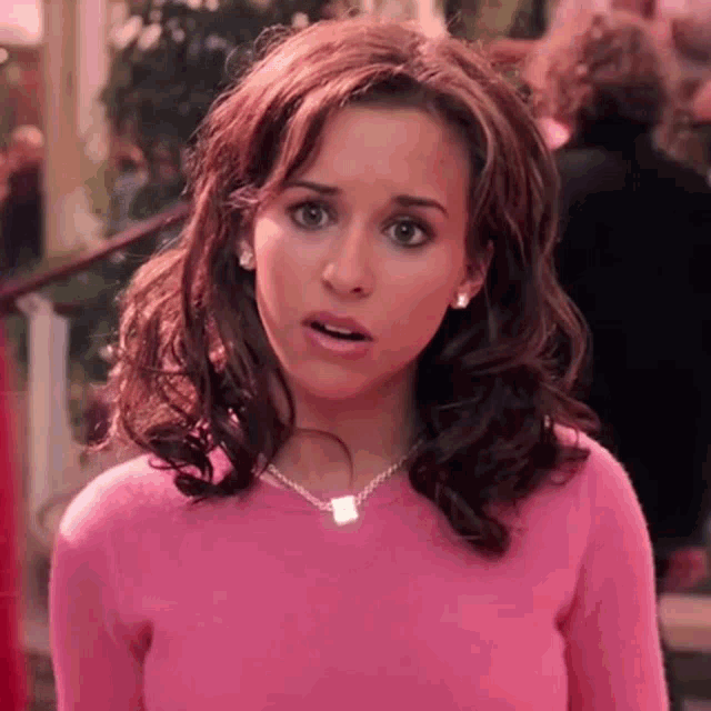 the woman is wearing a pink sweater and a necklace .