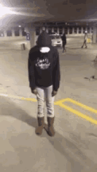 a person wearing a hoodie and boots is standing in a parking lot .