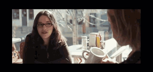 two women are sitting at a table with a cup of coffee