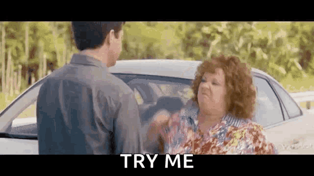 a man and a woman are standing next to each other in front of a car . the woman is yelling at the man .