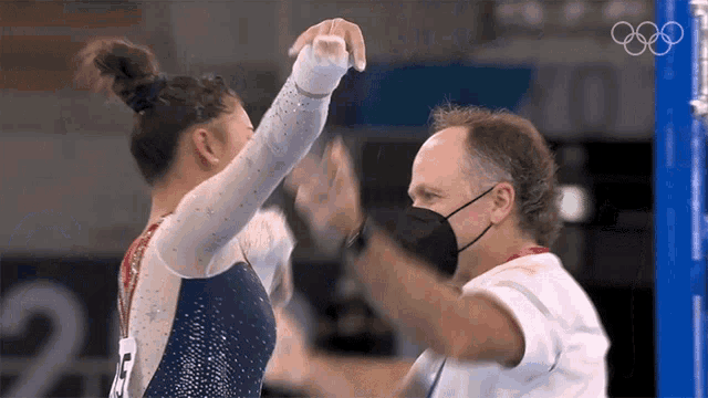 a man wearing a mask holds the hand of a gymnast