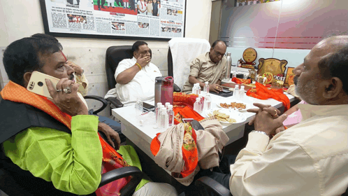 a group of men are sitting around a table and one man is talking on a cell phone that says lg