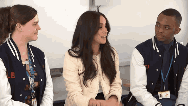 a woman wearing a jacket with the letter e on it sits with two other people