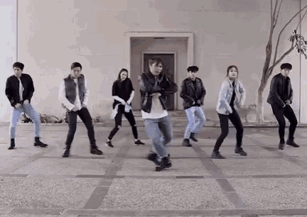 a group of young people are dancing in front of a building on a sidewalk .