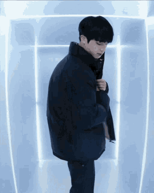 a man in a black jacket is standing in a room with blue lights behind him