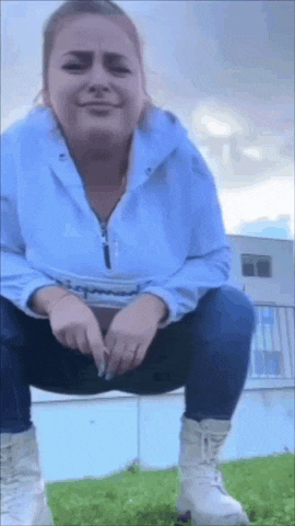 a woman in a blue jacket is squatting down on the grass .
