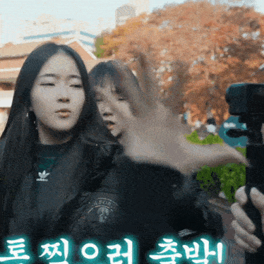a woman wearing an adidas jacket stands next to another woman holding a camera