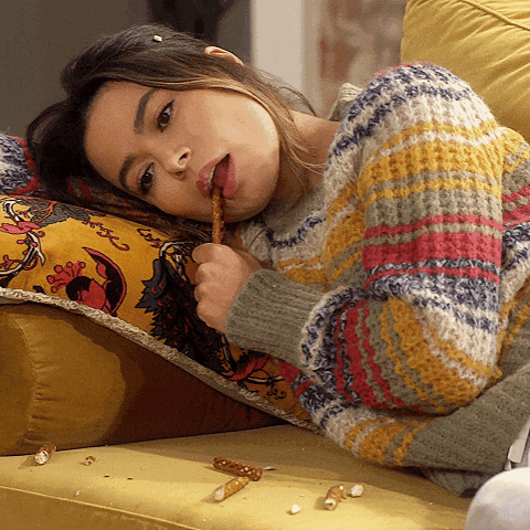 a woman laying on a couch with her tongue sticking out eating pretzels