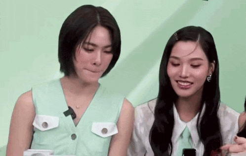 two women are sitting next to each other in front of a green background .