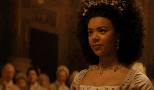 a woman wearing a tiara and a necklace stands in a dark room