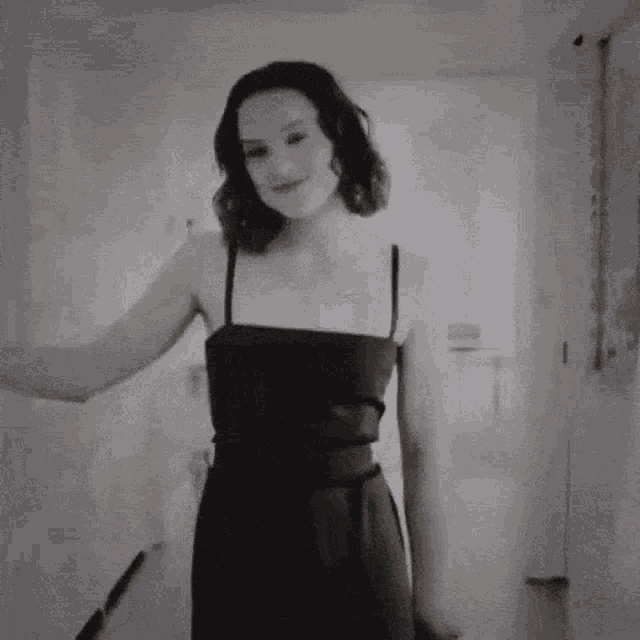 a woman in a black dress is sitting on a couch with her arms outstretched and giving the middle finger .