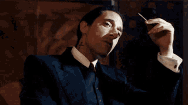 a man in a suit and tie is lighting a cigarette .