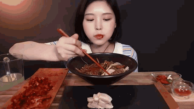 a woman is eating noodles with chopsticks and a piece of meat on a plate