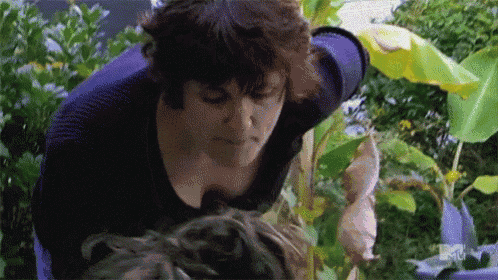 a woman in a purple shirt is standing in a garden with a mtv logo on the bottom right corner